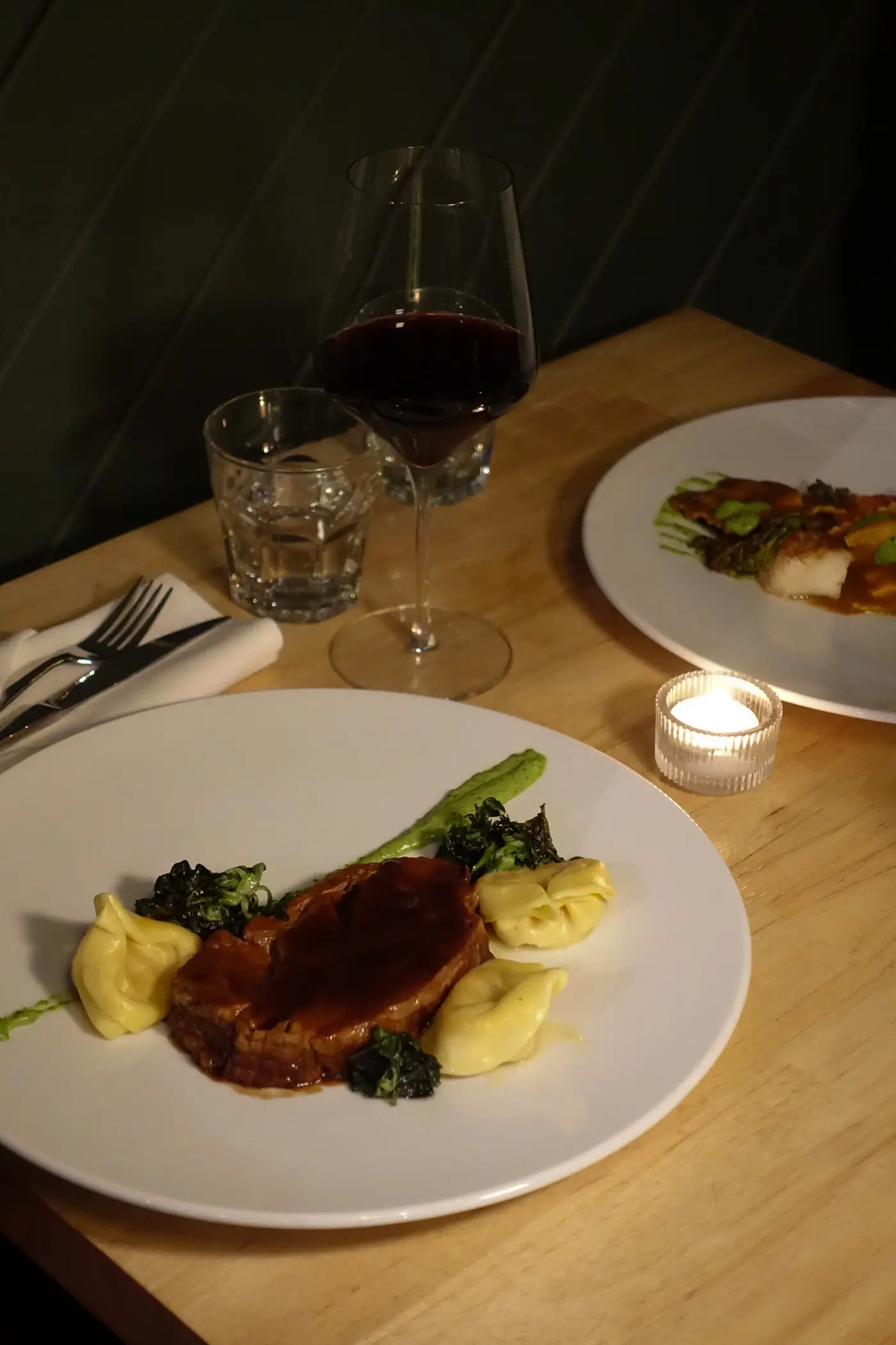 Bœuf braisé et pâtes sur une table de bois, verre de vin rouge et bougie