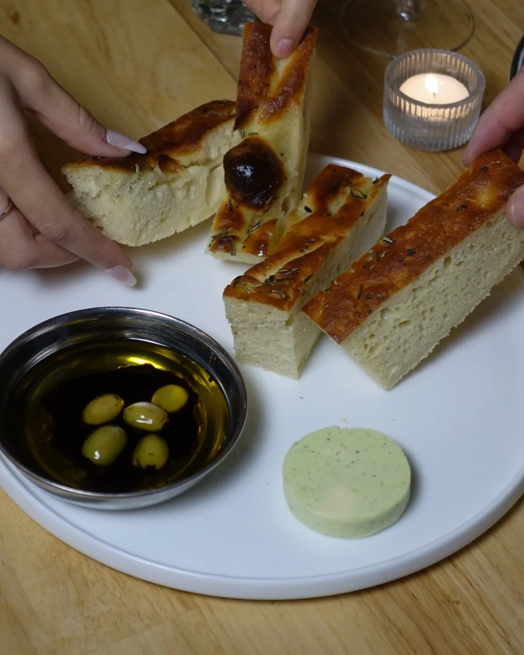 Mains qui partagent une focaccia maison, huile d’olive et olives